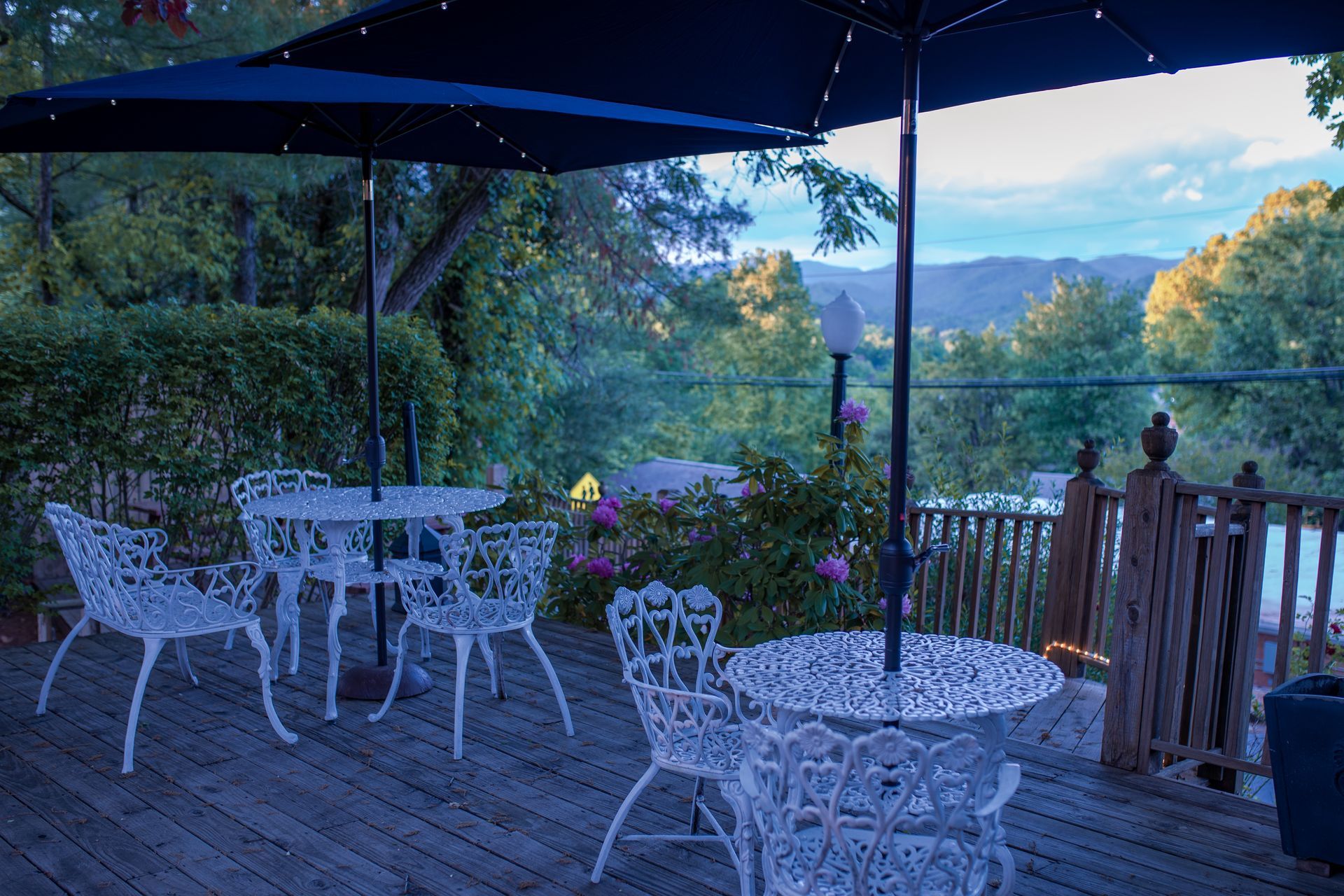 Outdoor café terrace with white tables and chairs, under a blue canopy, overlooking a scenic mountain valley.