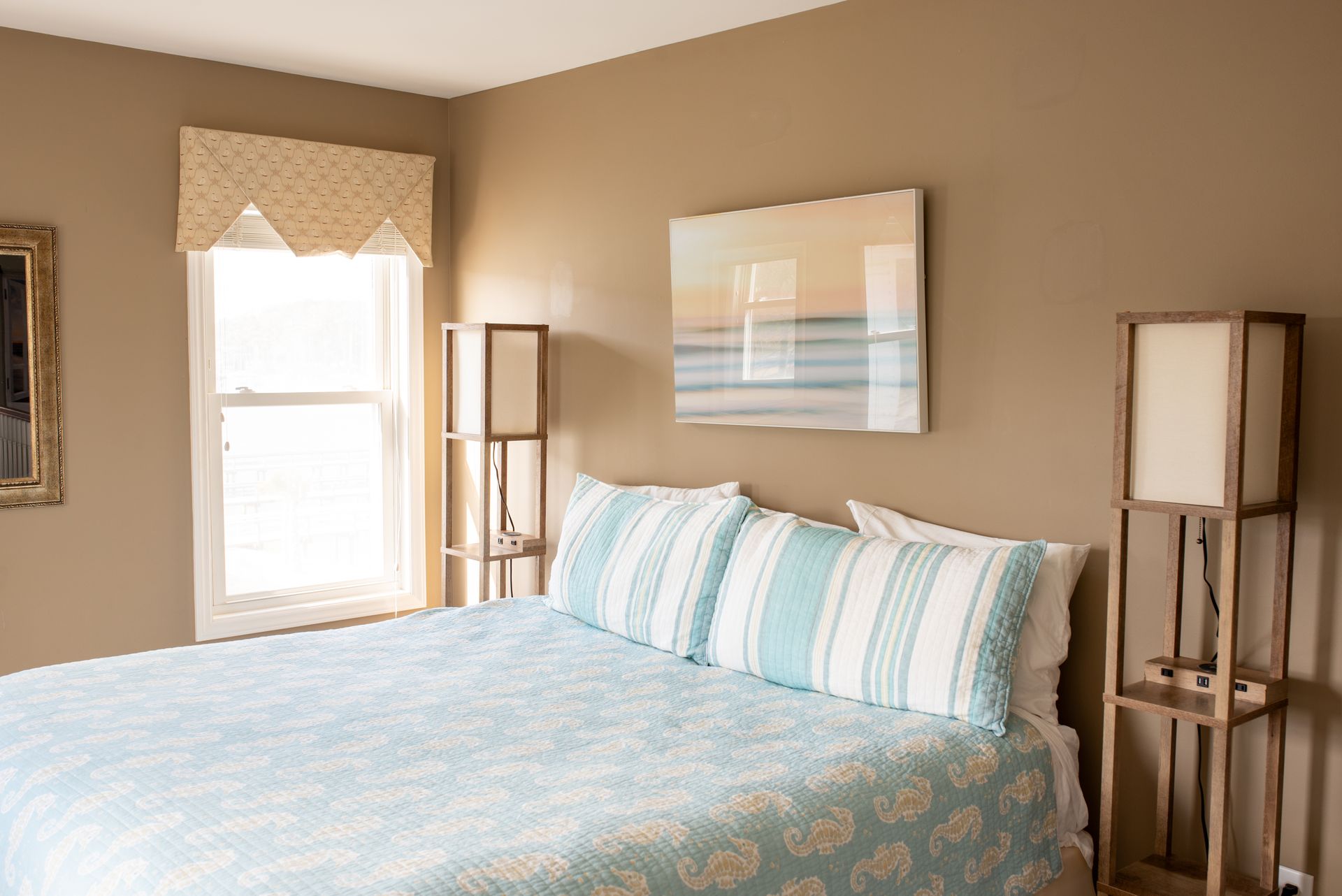 Bright bedroom with a bed, light blue bedding, two lamps, and a window with a woven shade