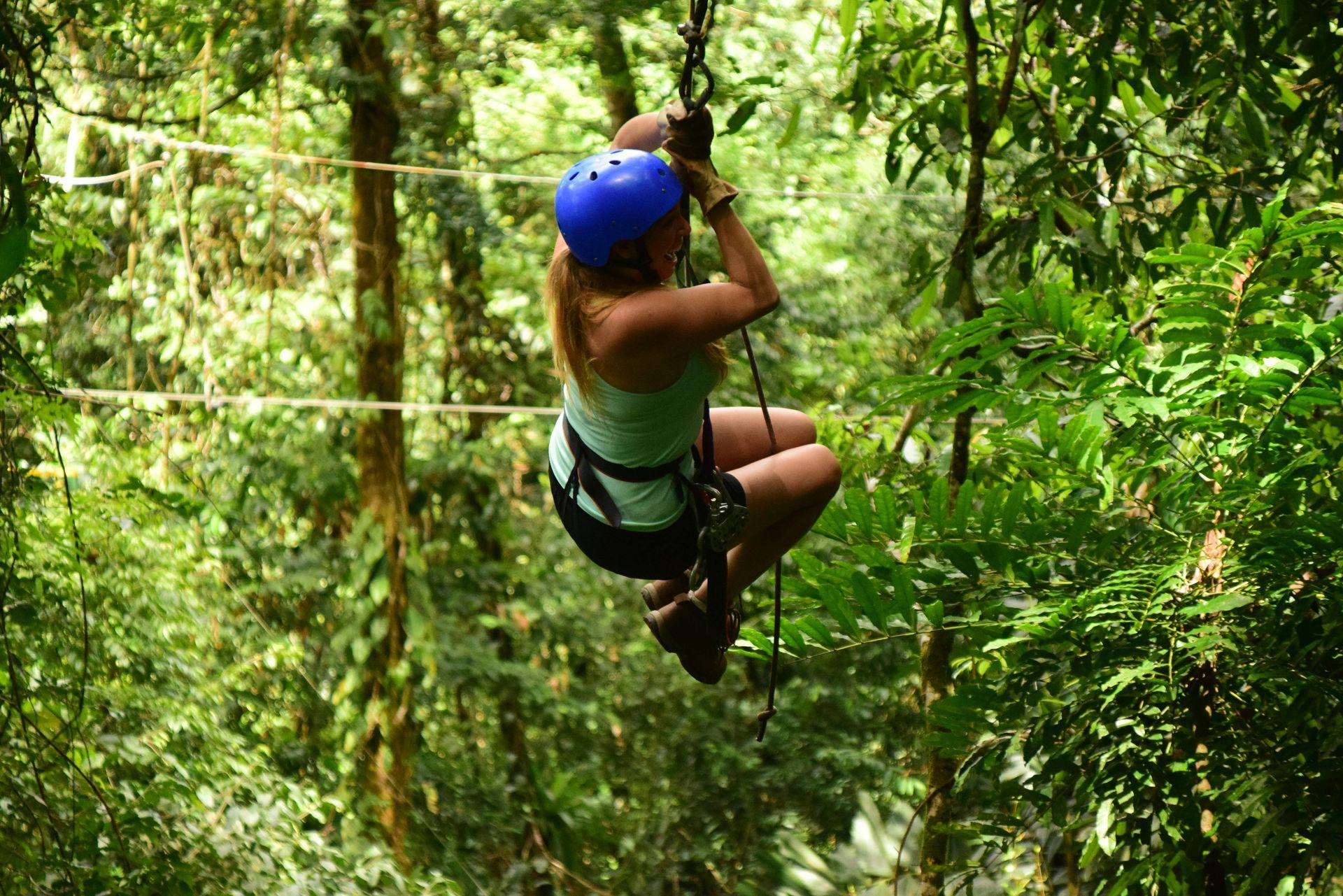 Person in a blue helmet zip-lining through a lush green forest