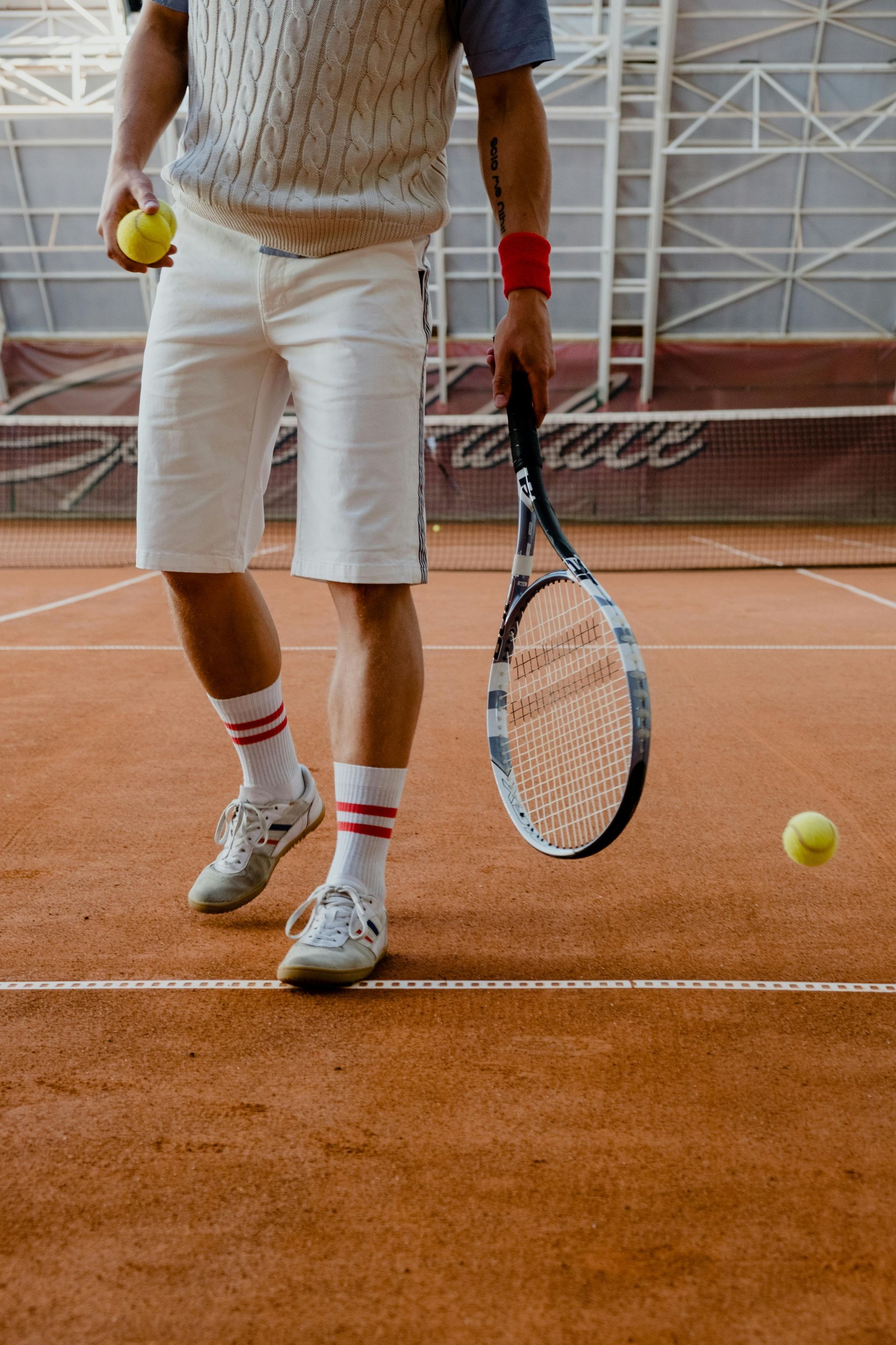 Tennis player on clay court holding racket and ball, with another ball bouncing nearby.