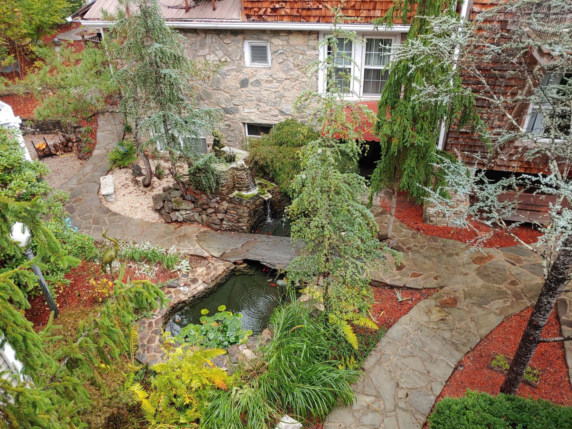 Stone courtyard garden with a small pond, lush greenery, and red-leaved shrubs beside a stone building