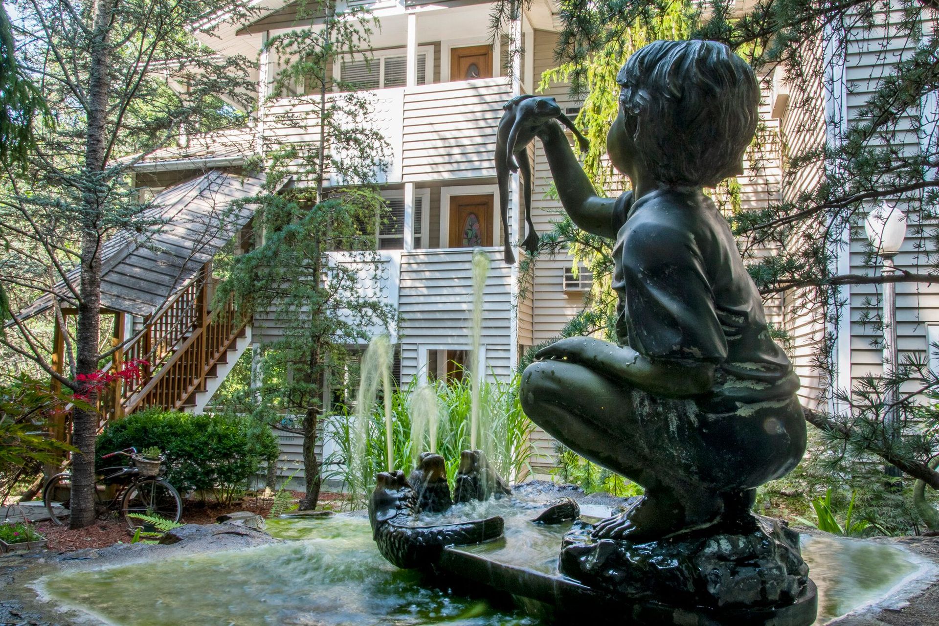 Bronze child statue beside a fountain in a leafy courtyard with apartment balconies