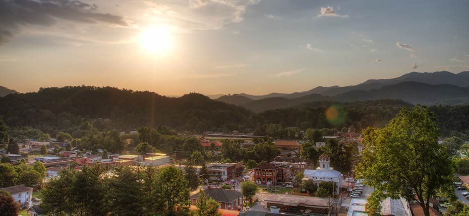 Sunset over a small town nestled among green hills and mountains, with warm light and scattered clouds