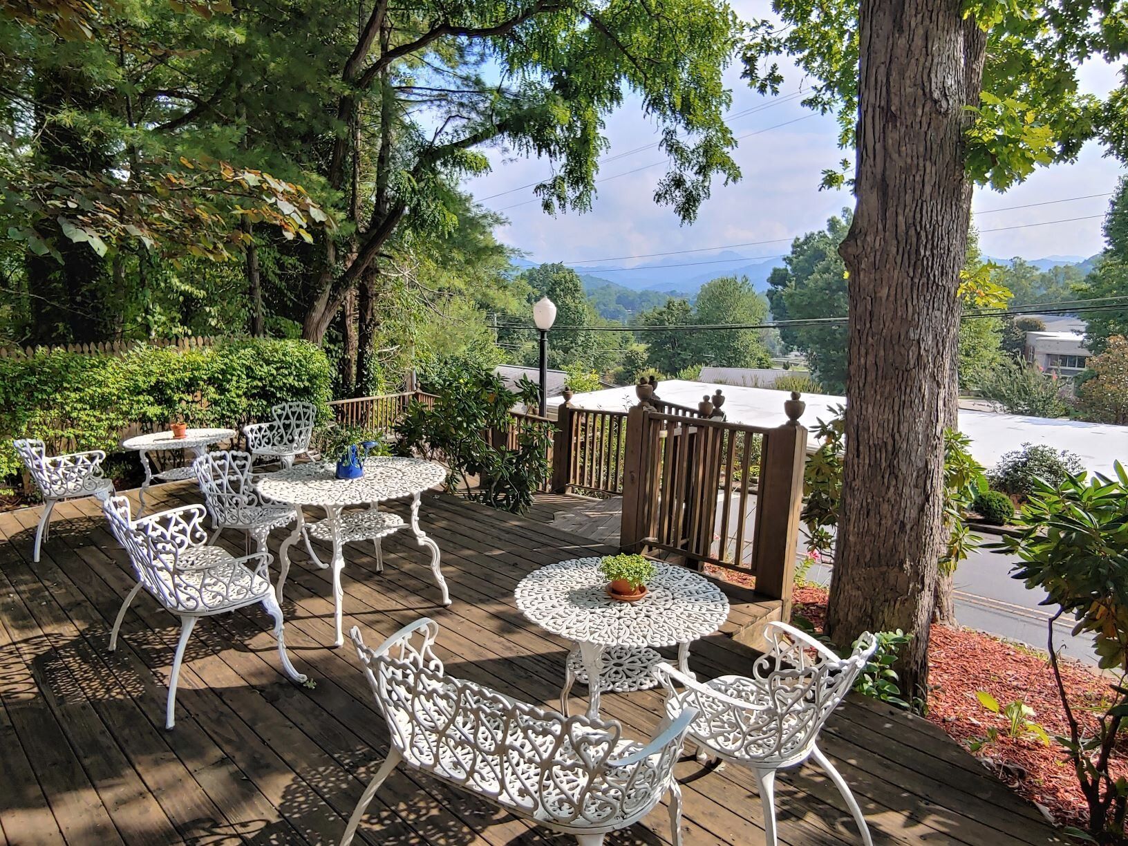 Patio tables and chairs under trees overlooking a scenic lake and mountains