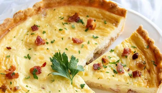 Sliced quiche with golden crust, creamy filling, bacon bits, and parsley garnish on a white plate