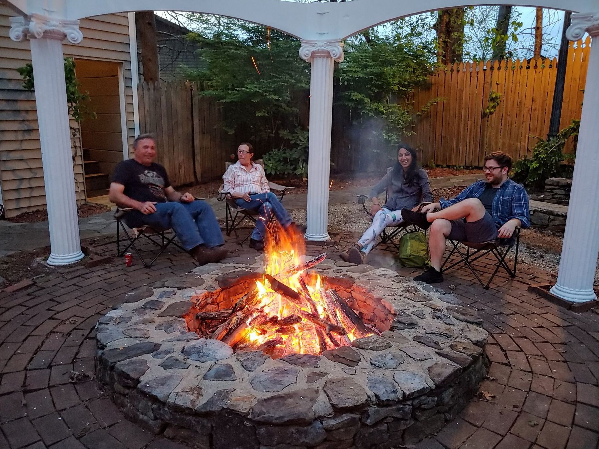 People seated around a glowing fire pit under a covered patio at dusk