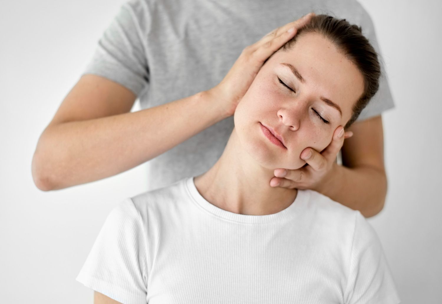 Person receiving a neck massage while seated, eyes closed, against a light background