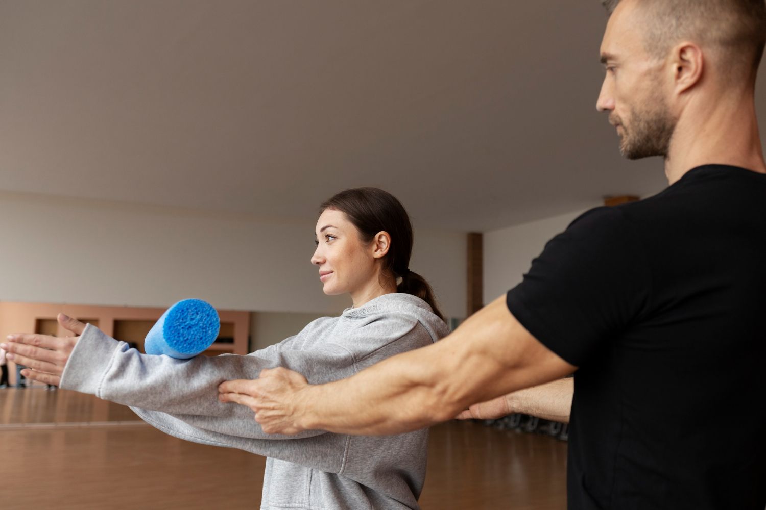 Two people stretching with a blue foam ball in a studio, focusing on arm extension.