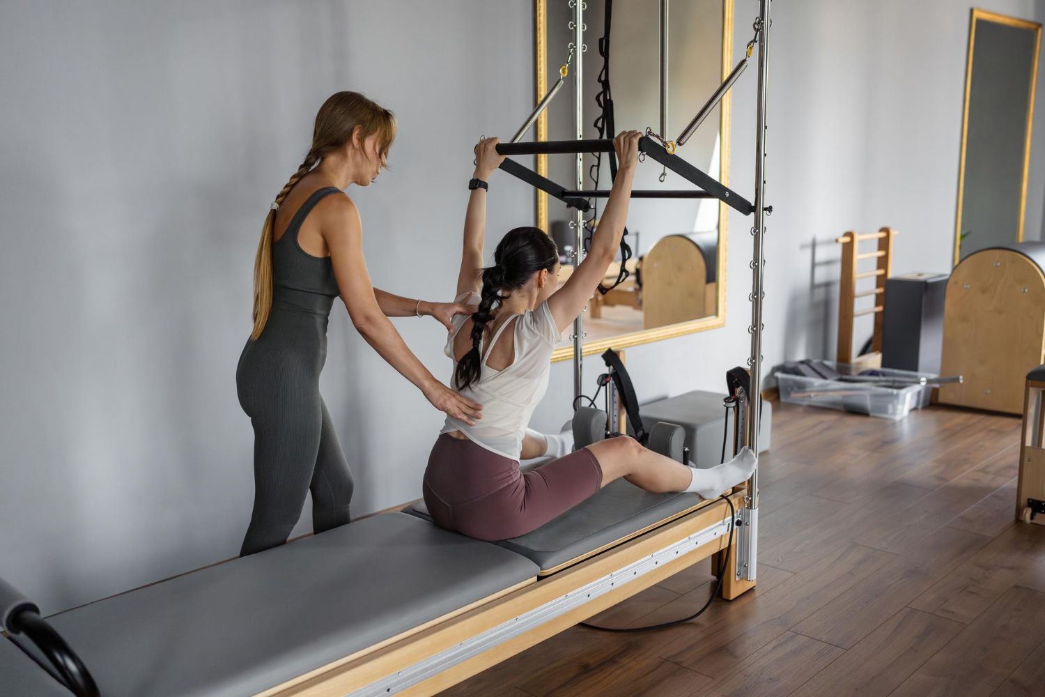 Pilates instructor assisting a woman on a reformer in a bright studio