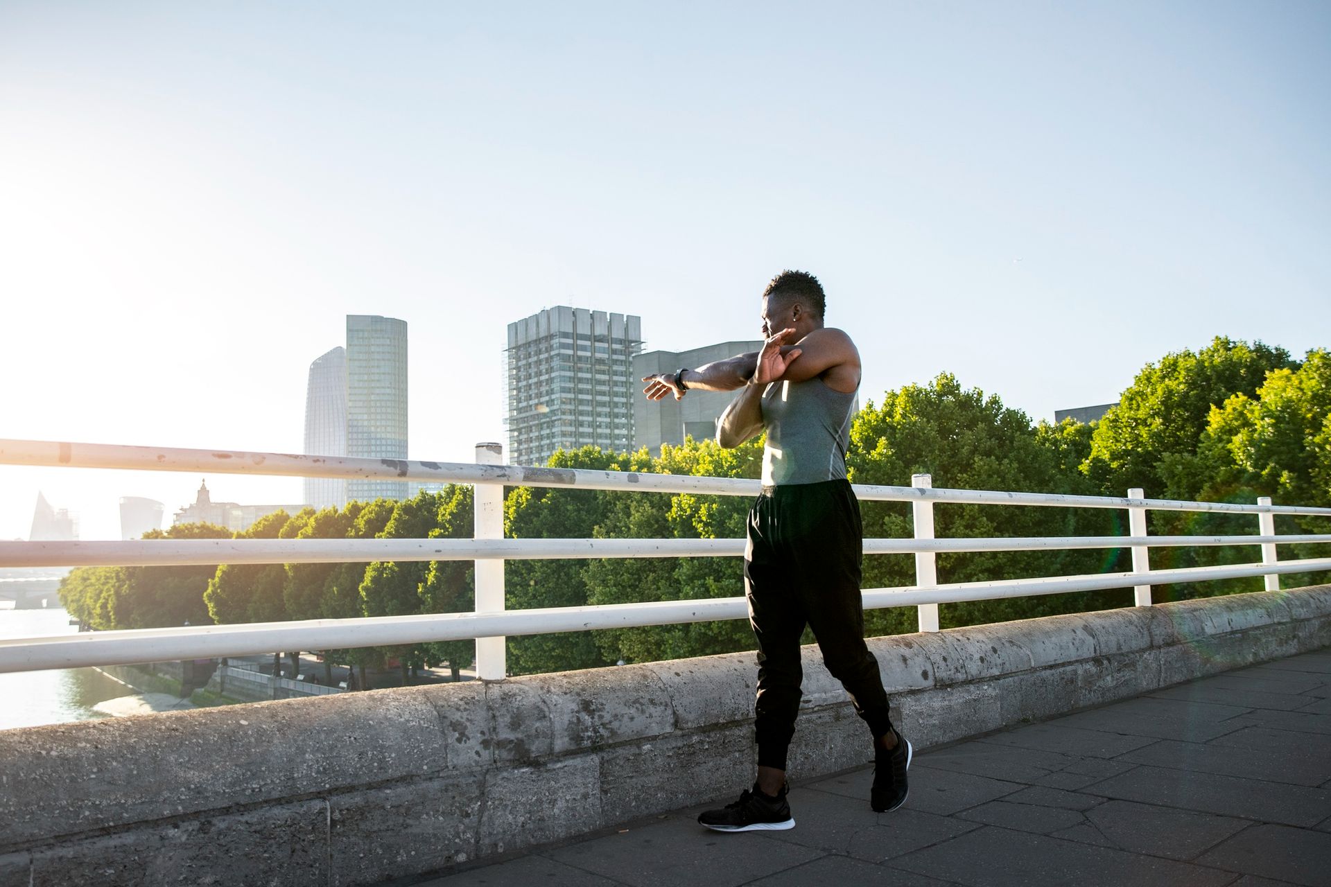 Person exercising on a bridge with city buildings and trees in the background