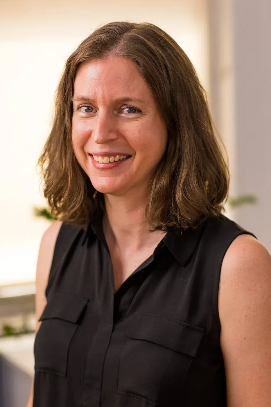 Portrait of a smiling person in a black sleeveless blouse against a softly blurred indoor background