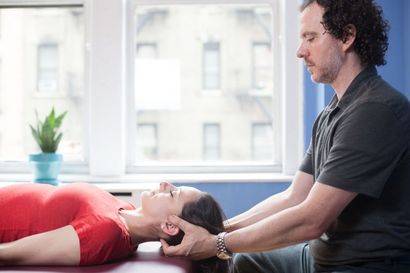 Person receiving a neck massage from a practitioner in a bright room near a window.