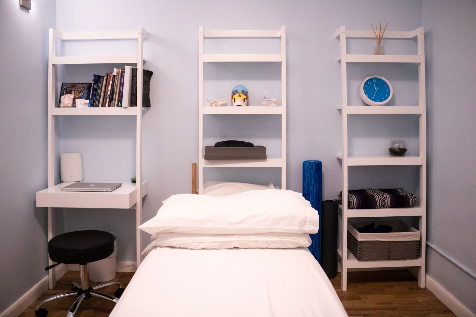 Small bedroom with a white bed, three white shelves, and a desk on the left.