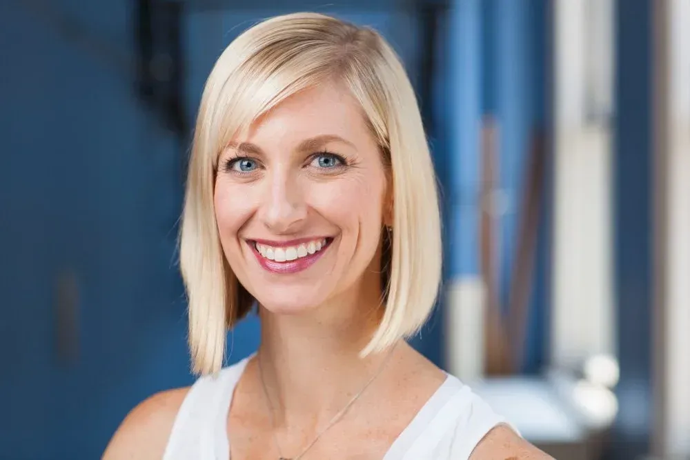 Smiling blonde woman in a white top against a blurred blue office background