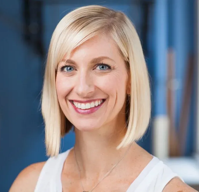 Smiling blonde woman in a white top against a blurred blue background