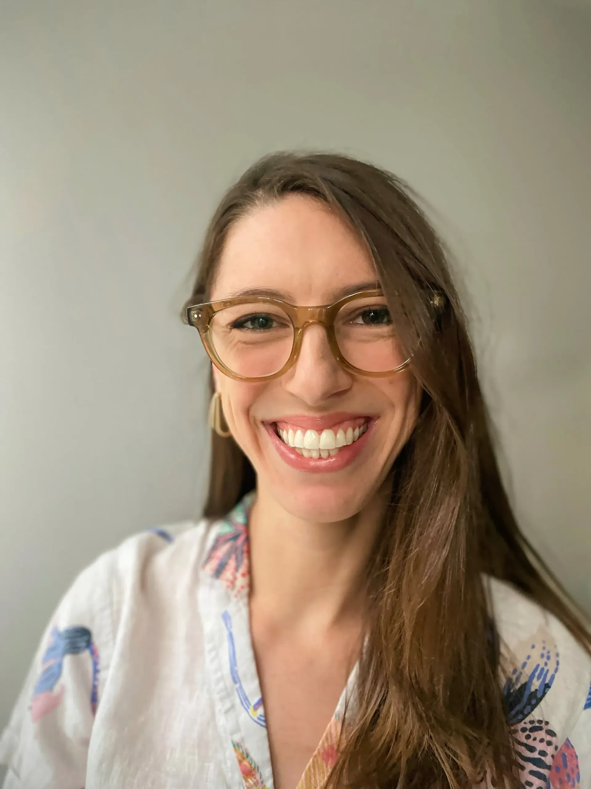 Smiling person with glasses in a light floral blouse against a plain background