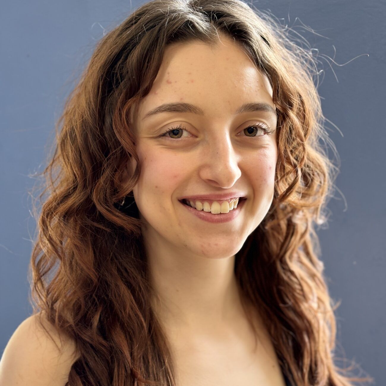 Smiling person with wavy brown hair against a blue background