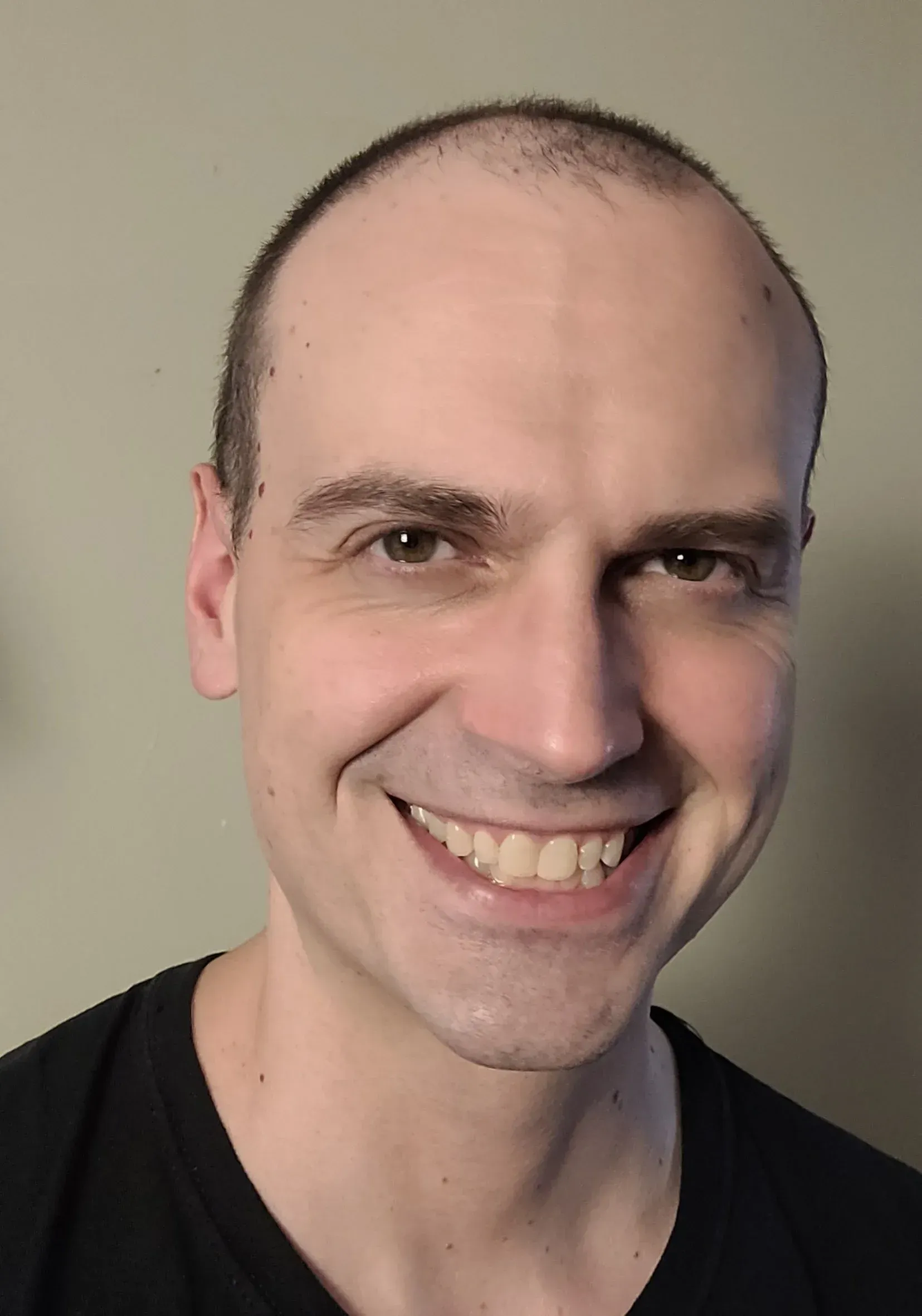 Smiling bald man in a black shirt against a plain beige background