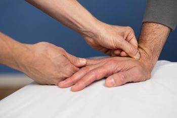 Hands receiving a wrist pulse check on a white medical bed