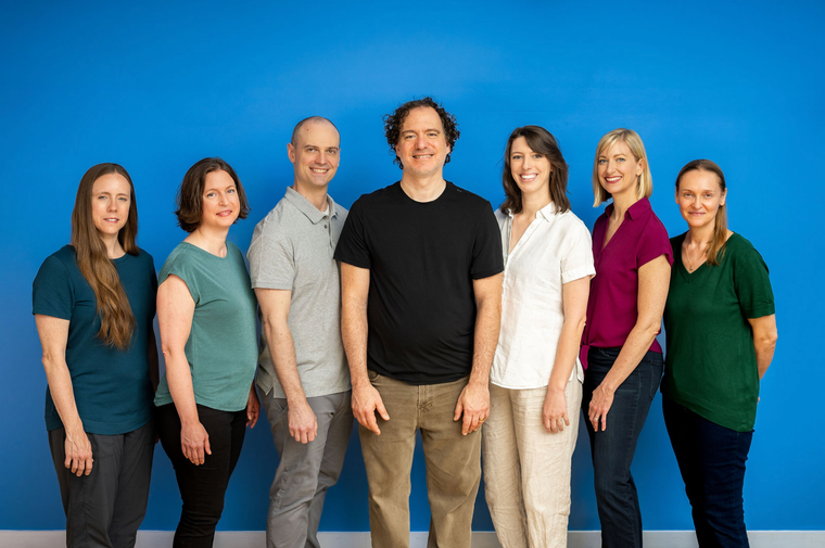 Five people standing together, smiling for a group portrait against a plain background