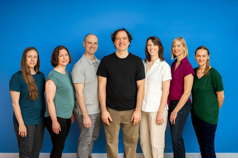 Five people standing together, smiling for a group portrait against a plain background