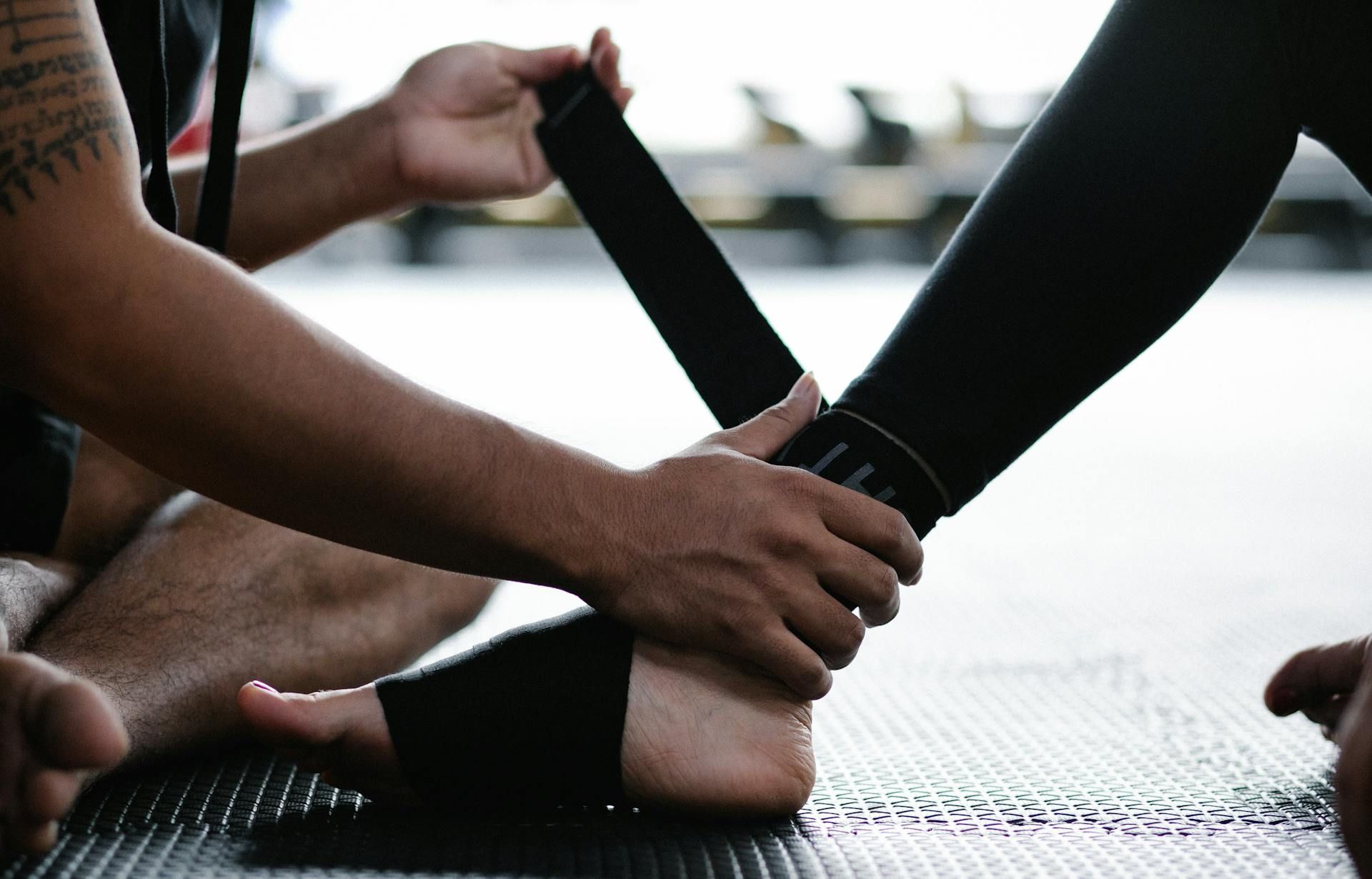 Person wrapping a black strap around an ankle on a gym mat