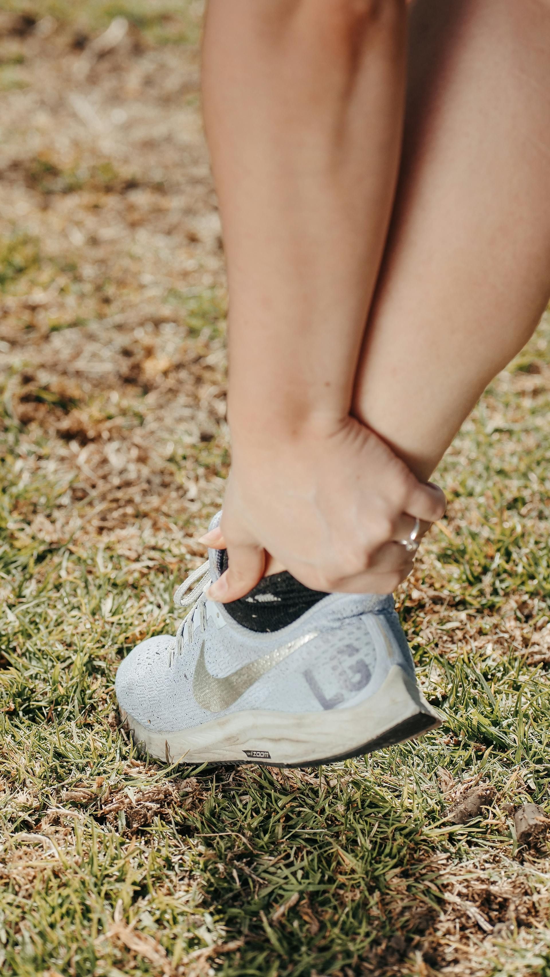 Hands tying the laces of a white running shoe on grass.
