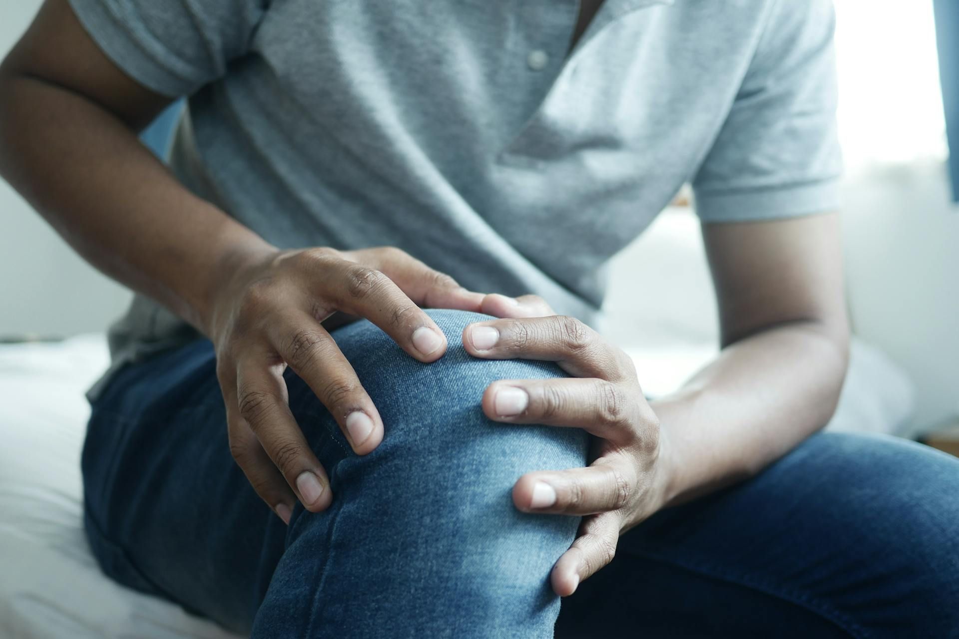 Hands clasped over a bent knee, suggesting knee pain or discomfort while sitting on a couch.