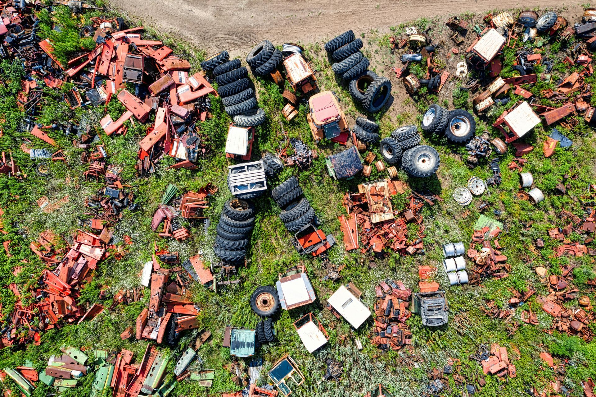 An aerial view of a junkyard scattered with rusted orange machinery parts, vehicle frames, and piles of black tires.