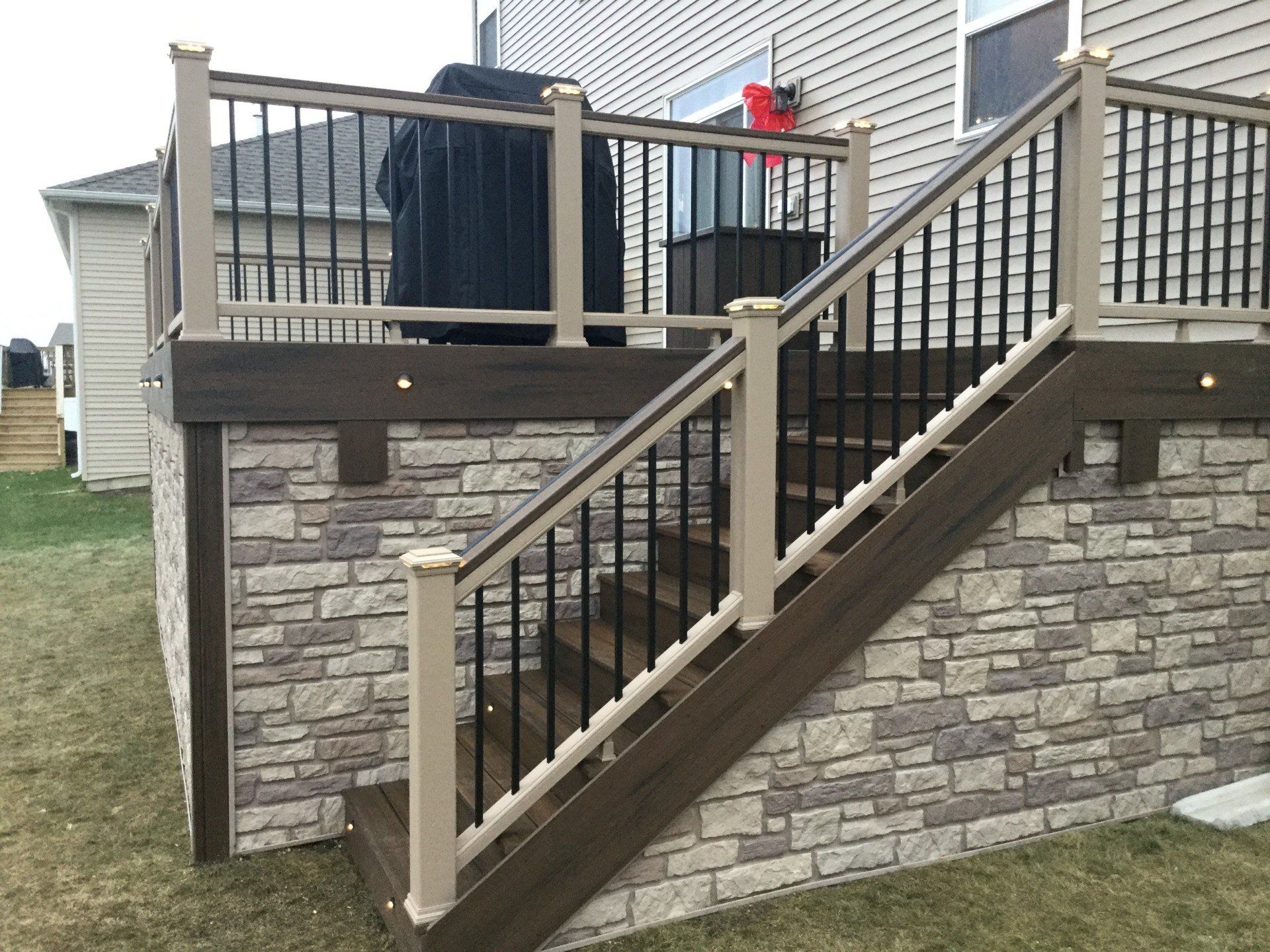 Stone-faced deck stairs with beige railings leading to an elevated wooden deck and patio.