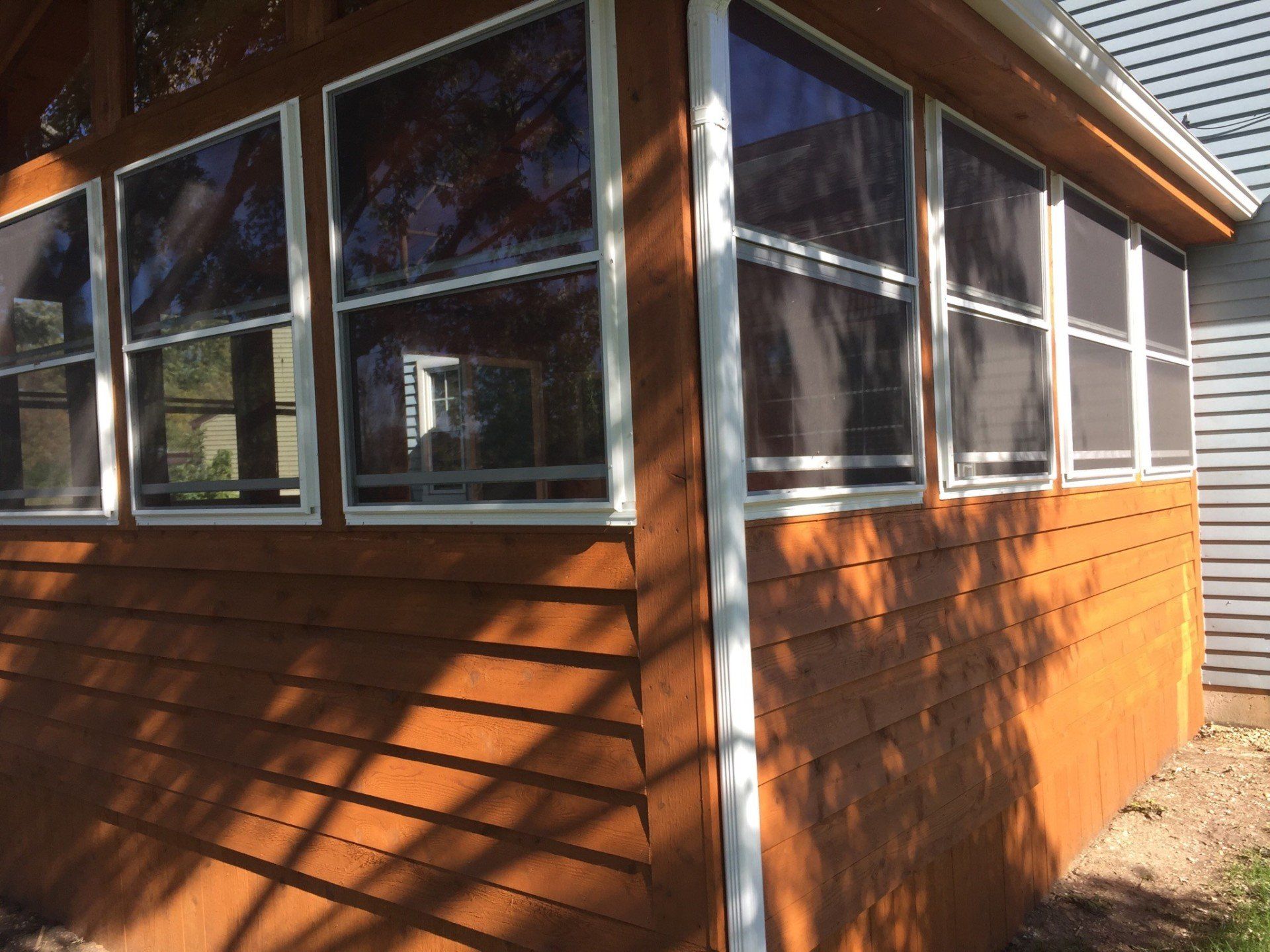 Wooden house exterior with large screened windows and orange-brown siding in sunlight
