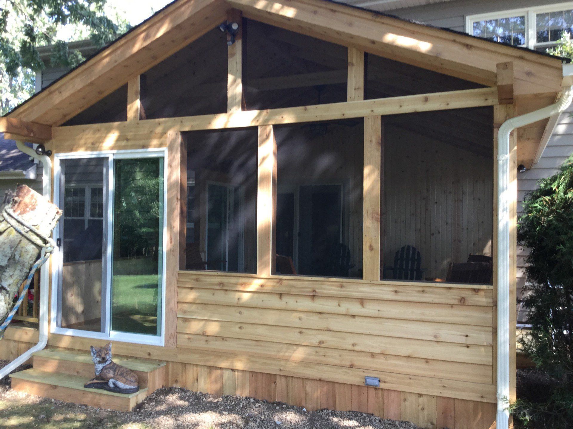 Wooden backyard shed or cabin with sliding glass door, windows, and a small deck.