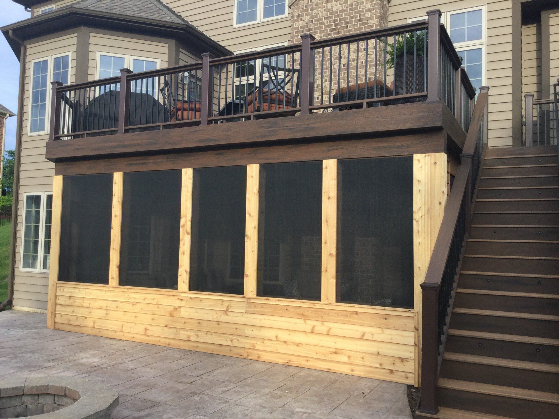 Wooden deck and screened porch attached to a stone house, with exterior stairs on the right.