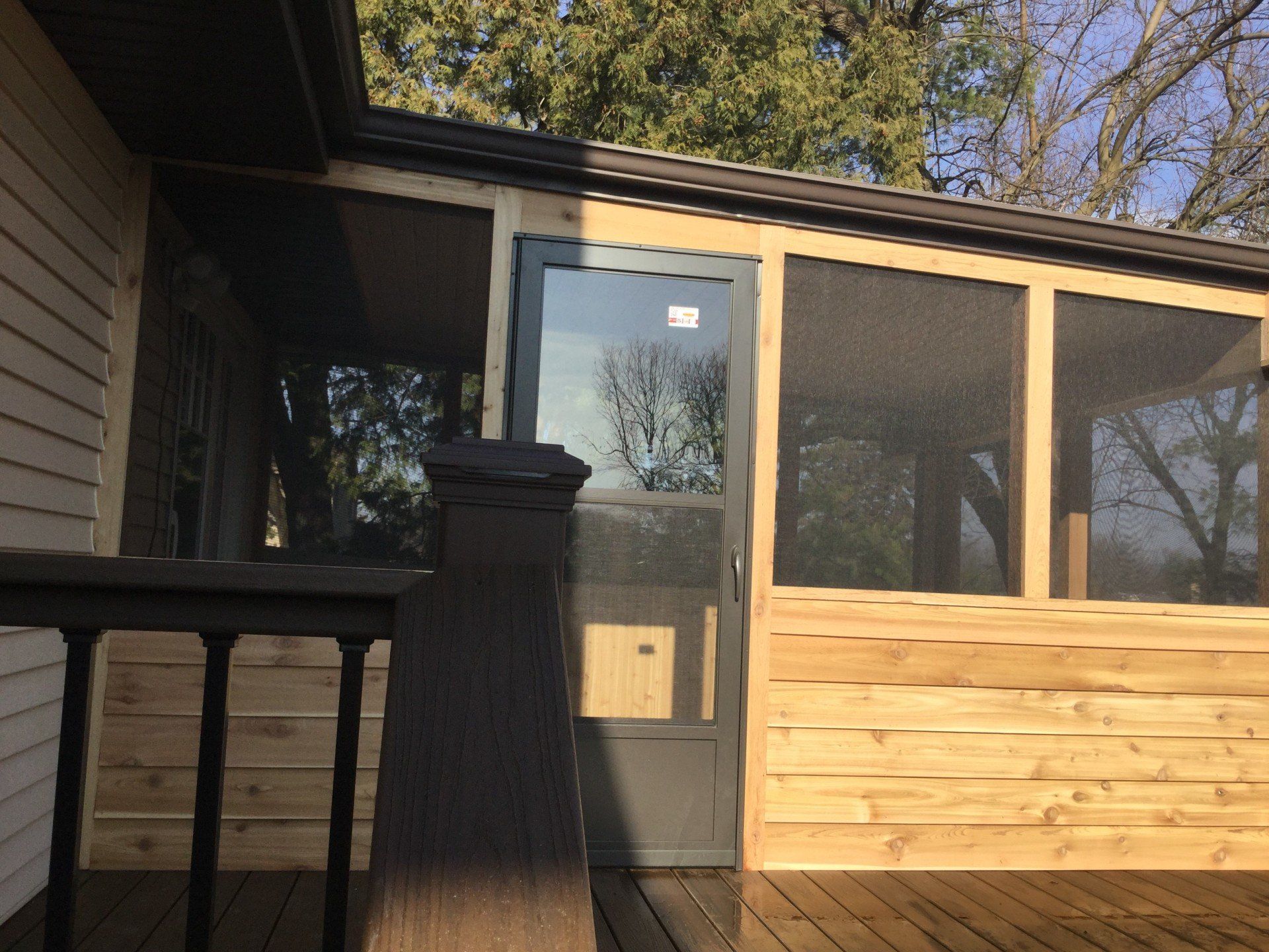 Porch with dark railing, glass door, and light wood siding on a house exterior