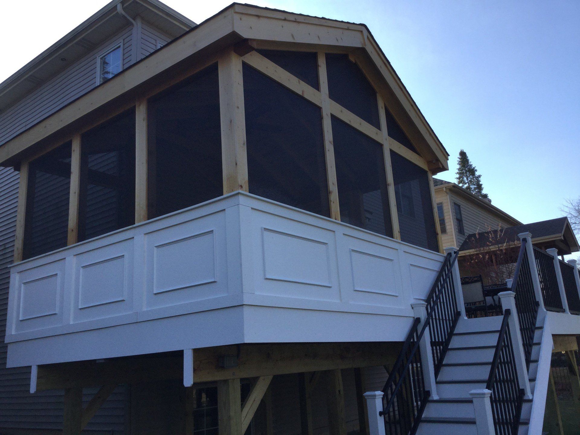House exterior with white siding and screened porch on stilts, viewed from below beside stairs