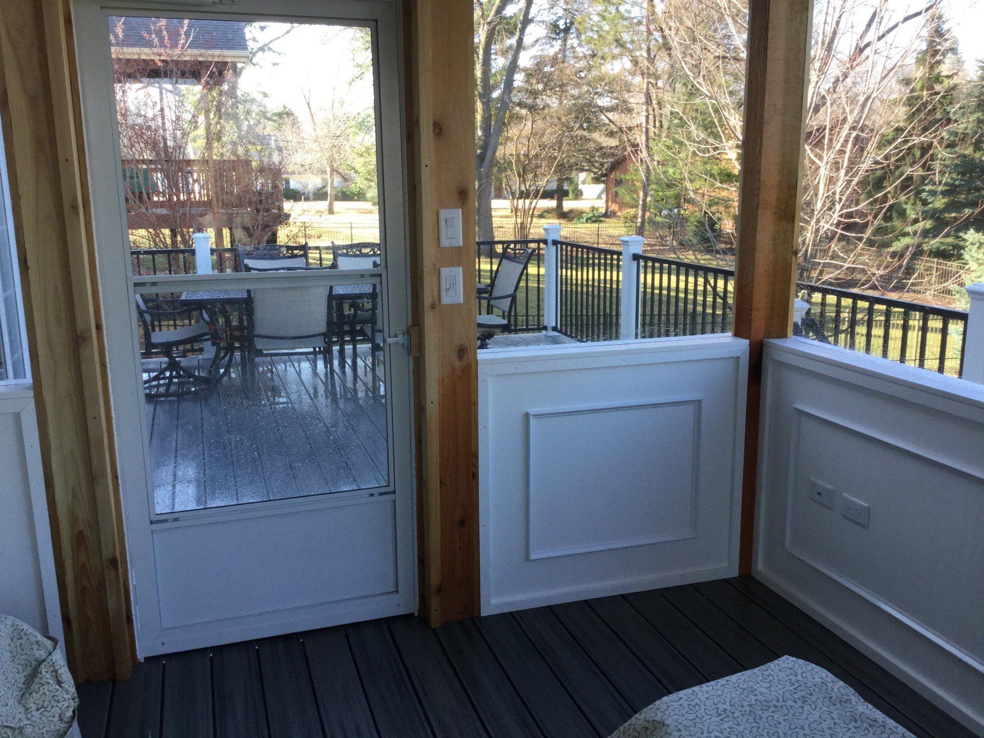 Covered porch with glass door, white railing, and outdoor patio furniture beyond the doorway.