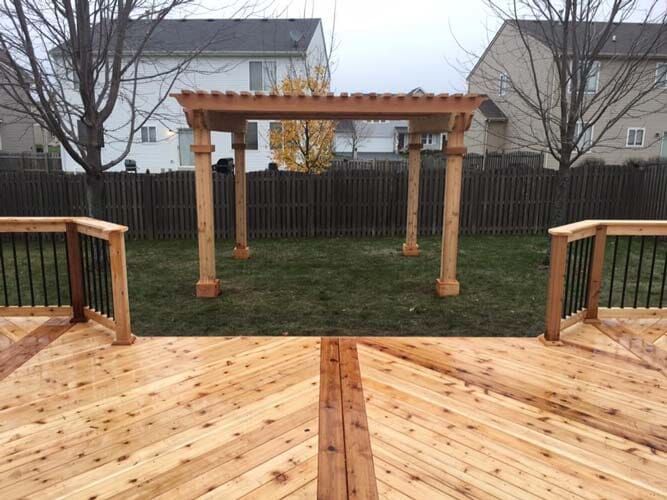Wooden deck overlooking a backyard with a pergola, fence, trees, and houses in the background