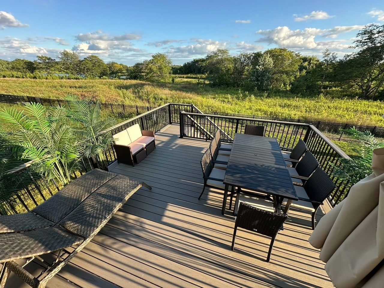 Patio deck with black table and chairs overlooking a sunny garden and fields