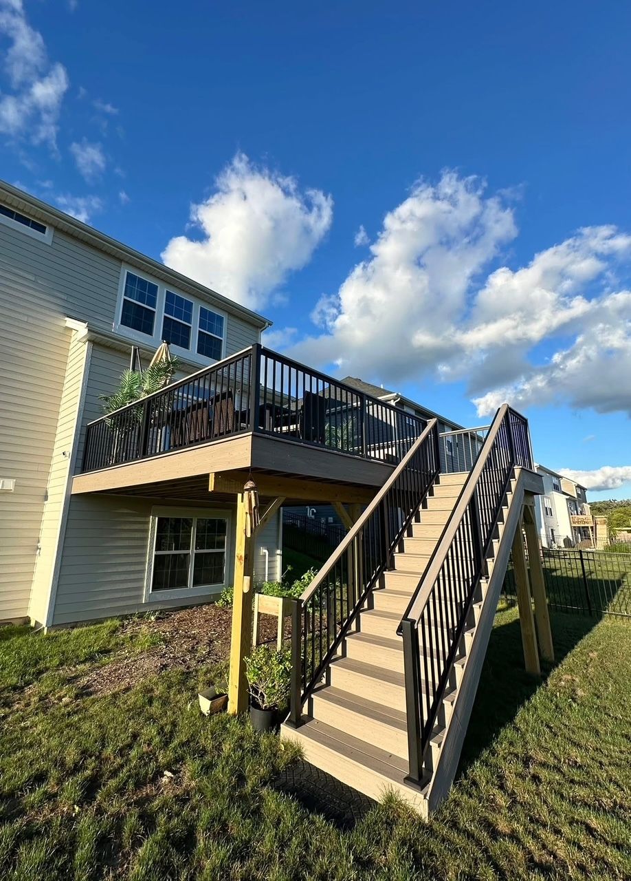 Apartment building with exterior wooden stairs and a deck under a blue sky with clouds