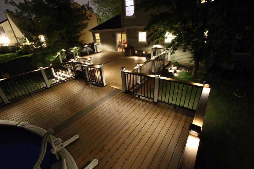 Nighttime wooden deck with railing and warm outdoor lights beside a house