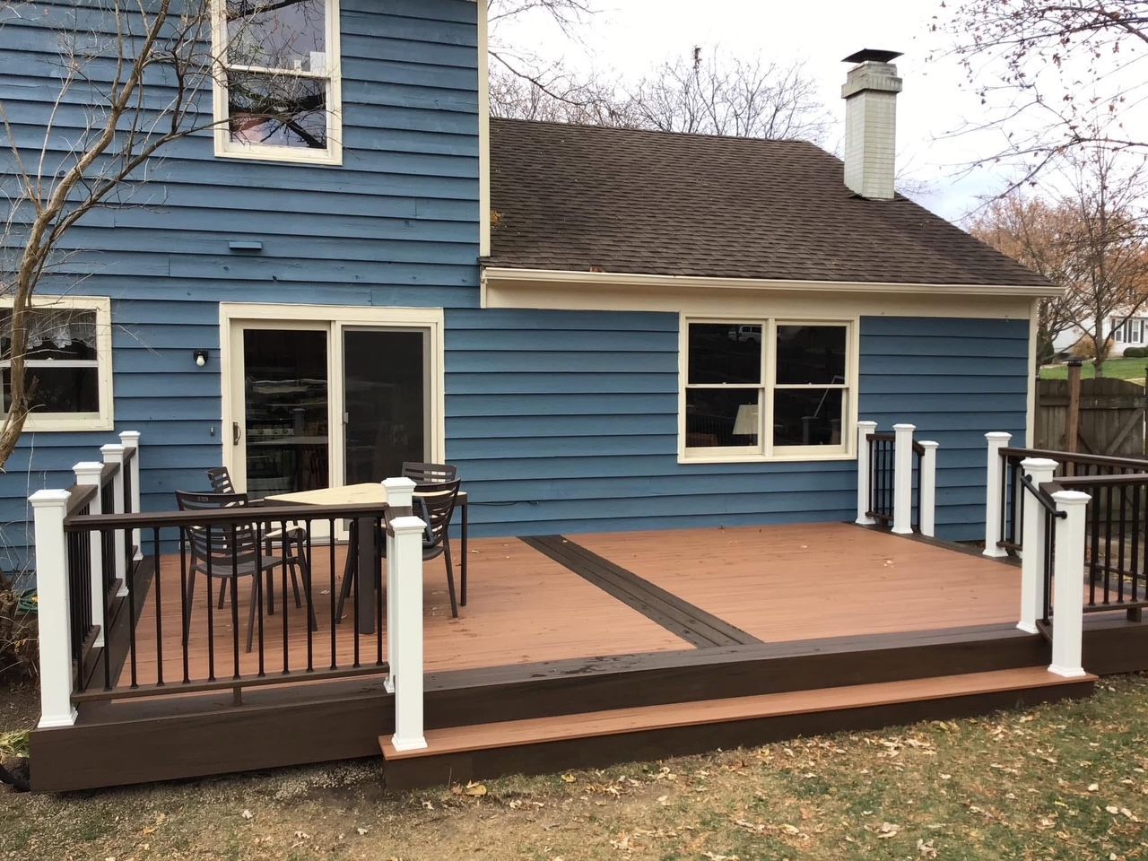Blue house with a raised wooden deck, black railing, and white posts in the backyard