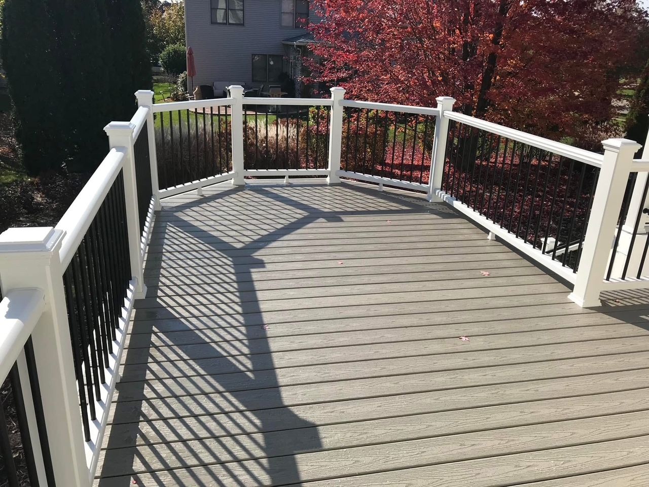 Curved wooden deck with white railings and long shadows in sunlight