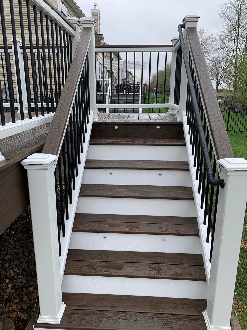 Outdoor staircase with white railings, black balusters, and snow-covered steps leading up to a deck.