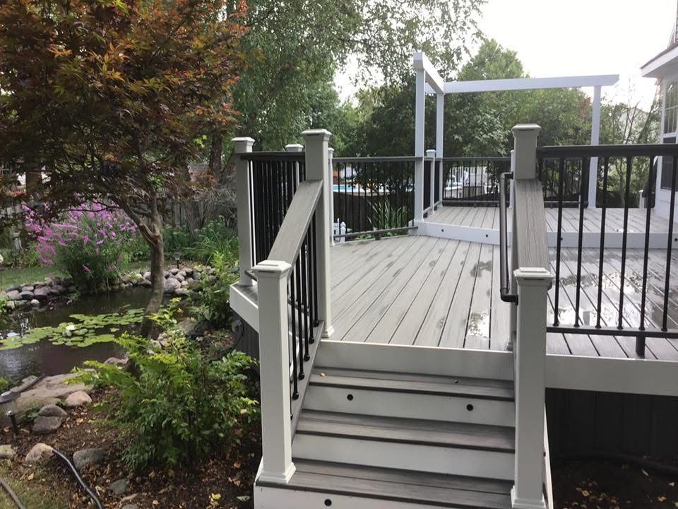 Wooden steps leading to a raised deck with black railings in a garden setting