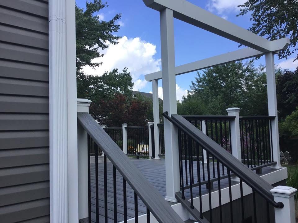 Front porch with gray siding, black railings, and open view of a yard under a cloudy sky