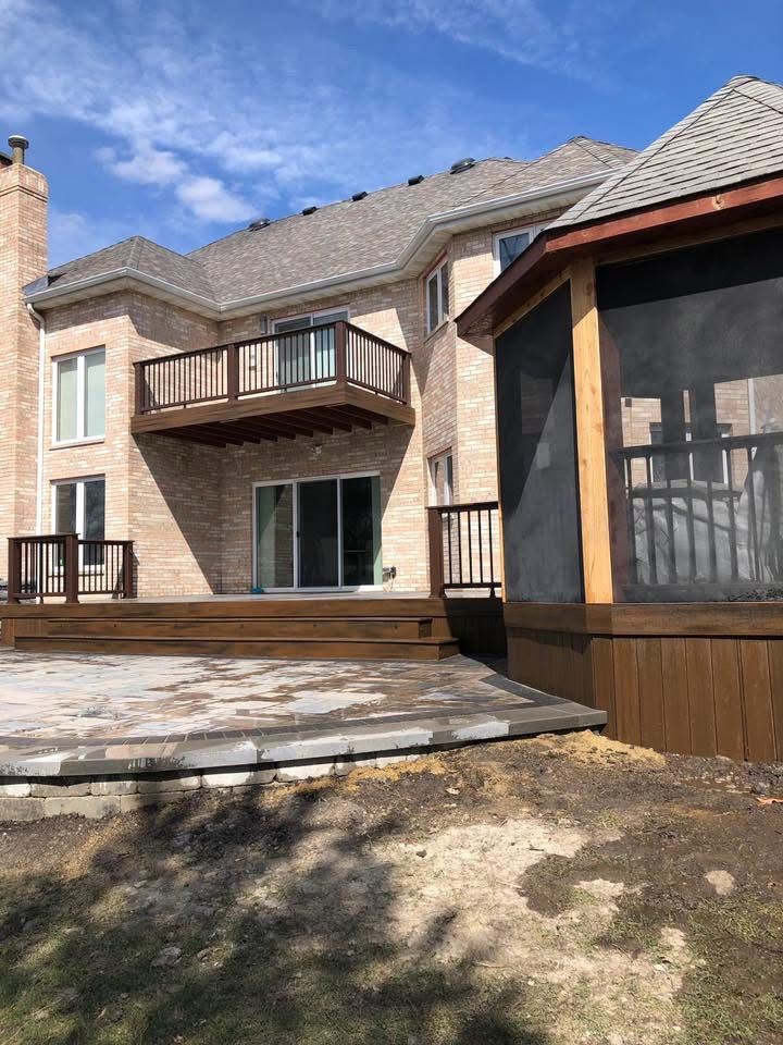 Large two-story brick house with a balcony, patio, and screened porch under a blue sky