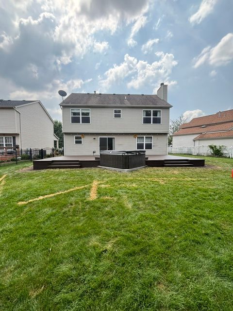 Backyard view of a two-story white house with a raised deck and green lawn under a cloudy sky