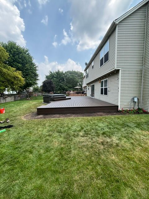 Backyard with white house and dark wooden deck, green lawn, trees, and partly cloudy sky