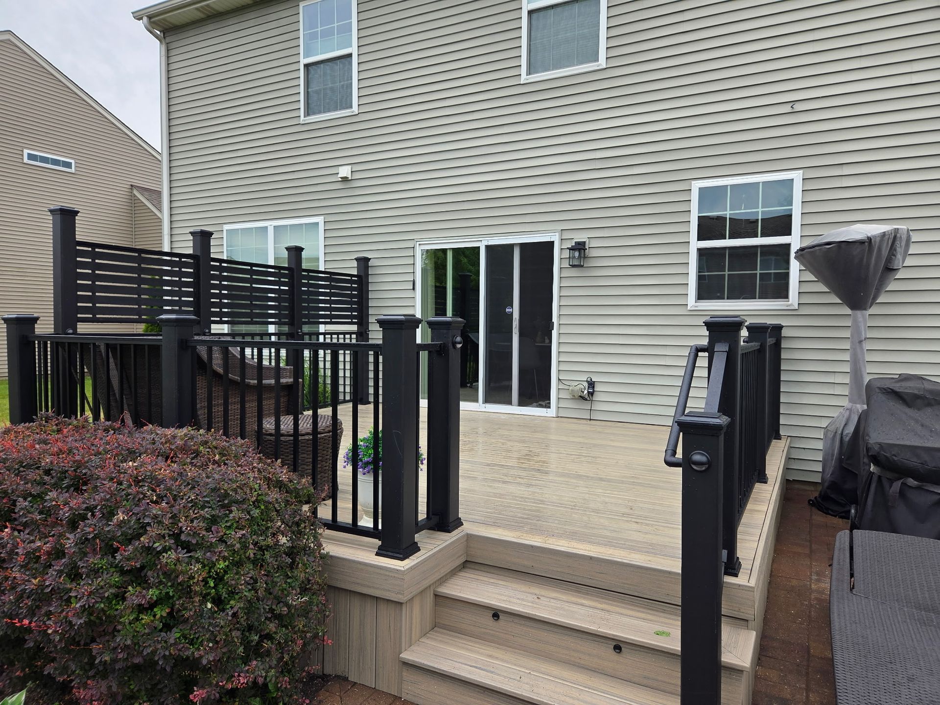 Backyard deck with black railing, steps, sliding glass doors, and a grill beside a townhouse.