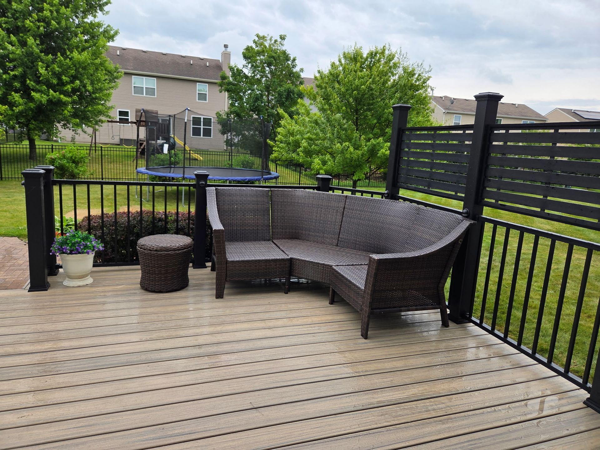 Backyard deck with wicker seating, fire pit, and black railing overlooking townhomes